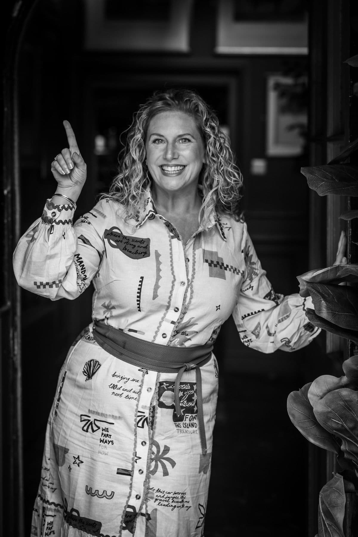 Tanya in a doorway, pointing up and smiling, in black and white